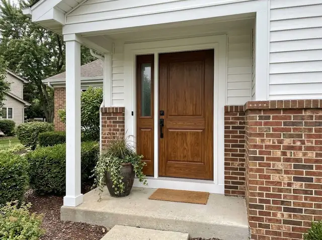 Newly installed stained wood front door with white trim on a brick home (illustration)