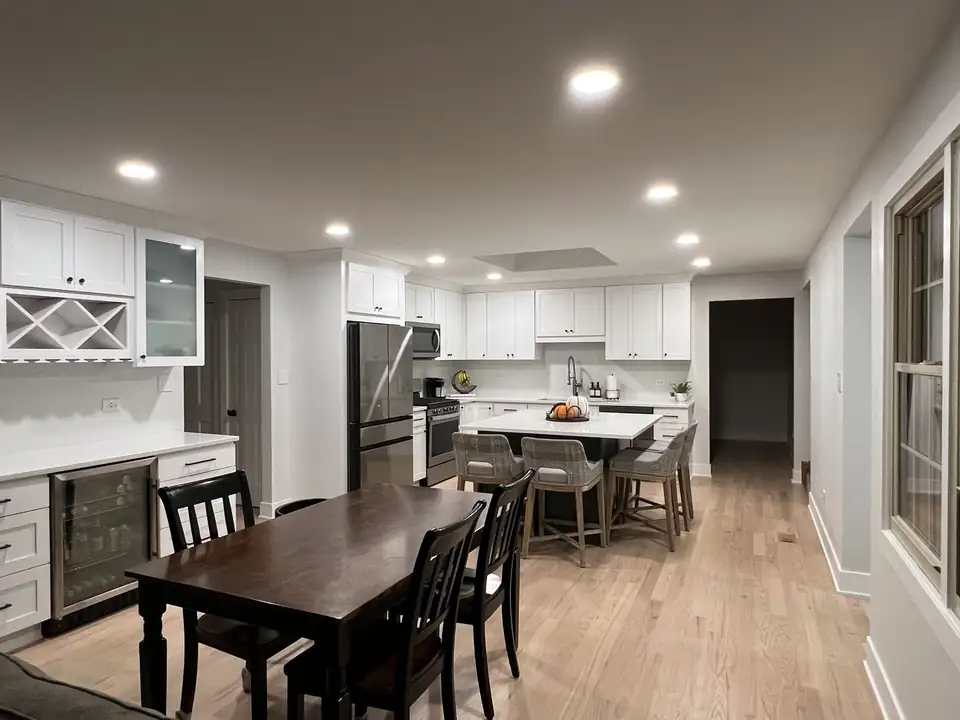 Open white kitchen with an island, recessed lights and a wood-look floor, an example of kitchen and bath remodeling in Batavia, IL from DMP Remodels