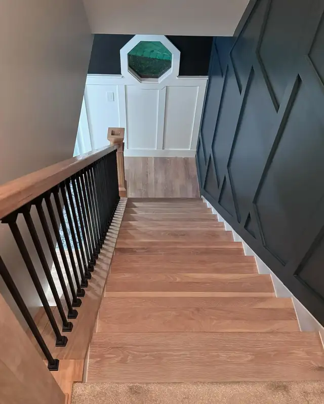 Staircase with wood treads, black iron balusters and a black geometric trim accent wall